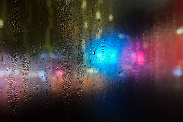 Rain drops on windshield glass window with road light bokeh, Colorful light city night life in a rainy day abstract background, water drop on the glass, storm raining driving with blur focus concept.