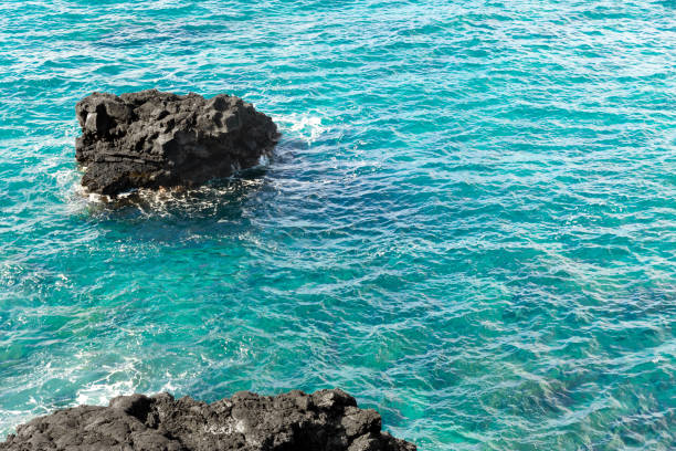Black volcanic rocks formed from lava in the turquoise waters of the pacific ocean. Big Island, Hawaii, the USA.