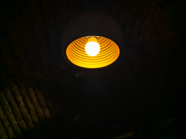 istock Modern round yellow lamp with warm light, orange LED shining light bulb hanging from ceiling of black construction in the dark room, with copy space. 2192587978
