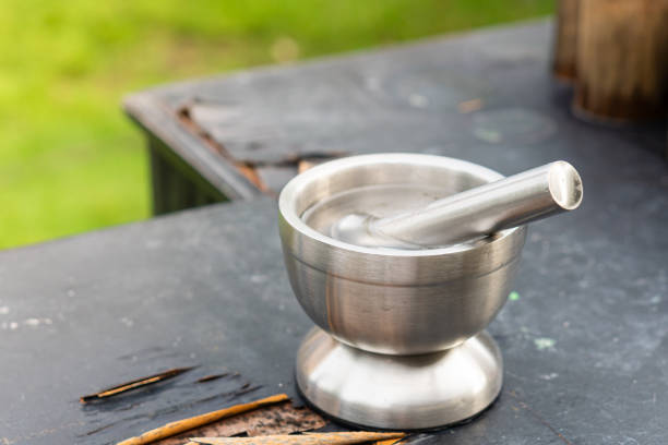 A stainless steel mortar and pestle set placed on a weathered black table. The mortar is round with a smooth surface, and the pestle is resting inside it. The background features