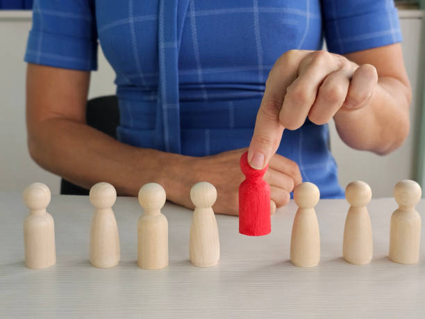 istock Wooden figures in a selection process highlighting a red figure in a professional setting 2192600800