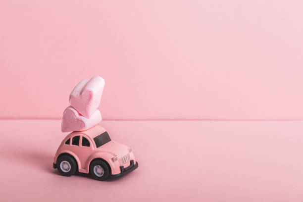 Small pink car model with two heart-shaped marshmallows on a pink background. Concept for Valentine's Day.