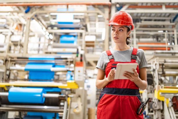 istock Focused female worker checks tablet for processes in expansive modern manufacturing plant. 2192613346