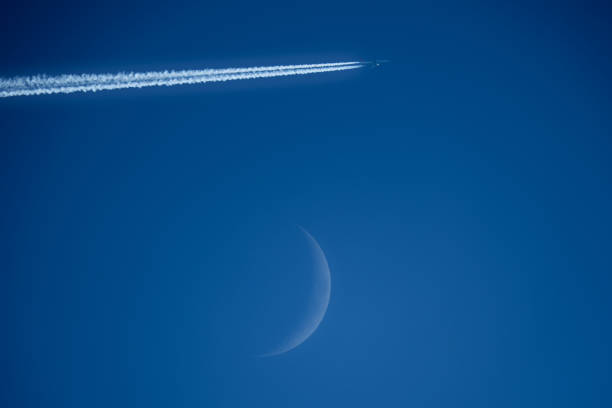 moon and airplane in the blue sky with contrail in the foreground