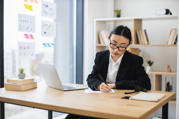 istock Focused Asian businesswoman writing notes at modern office desk 2192621708