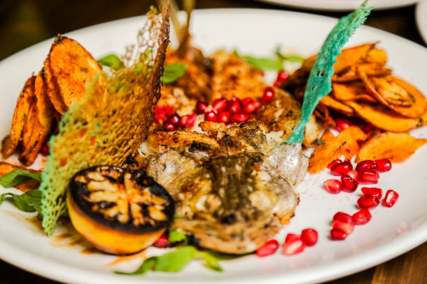 A beautifully presented gourmet dish features grilled fish, sweet potato slices, fresh pomegranate seeds, and colorful garnishes, showcasing culinary artistry.