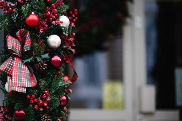 A detailed view of a Christmas garland decorated with red and white ornaments, plaid ribbons, pinecones, and berries. The holiday decoration creates a warm and festive atmosphere against a blurred background.