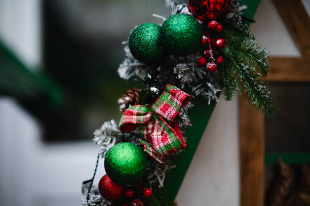 A detailed view of a Christmas garland decorated with red and white ornaments, plaid ribbons, pinecones, and berries. The holiday decoration creates a warm and festive atmosphere against a blurred background.