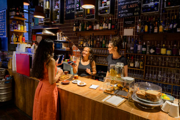 Mid adult indigenous Australian woman, and 17 year old daughter, working in family owned cafe, female customer making contactless paying for food and drink using cell phone