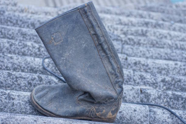 one old dirty black tarpaulin leather boot stands on the gray floor on the autumn street
