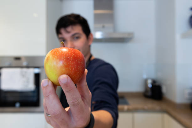 Defocused man holding an apple in his kitchen with copy space, natural food
