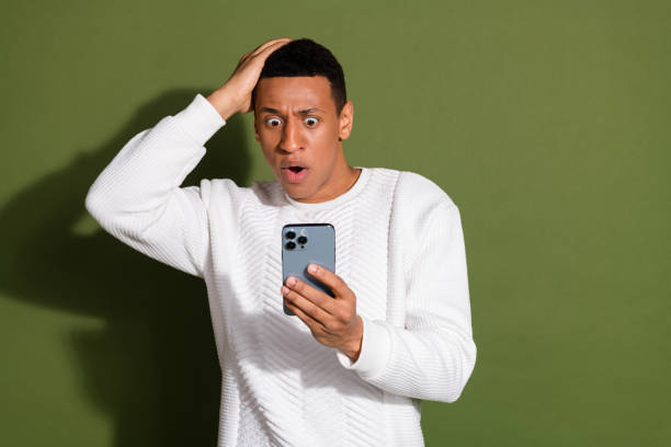 istock Young man in white sweater expressing shock while looking at smartphone against khaki background, highlighting surprise and emotion 2192645836