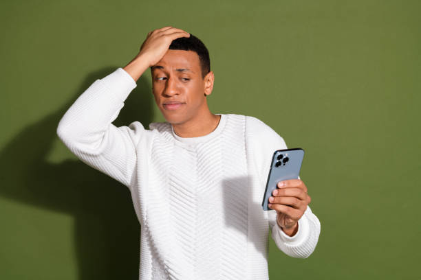 istock Young man in a sweater looks puzzled at smartphone against khaki backdrop, showcasing modern style and mixed heritage in casual setting 2192645838