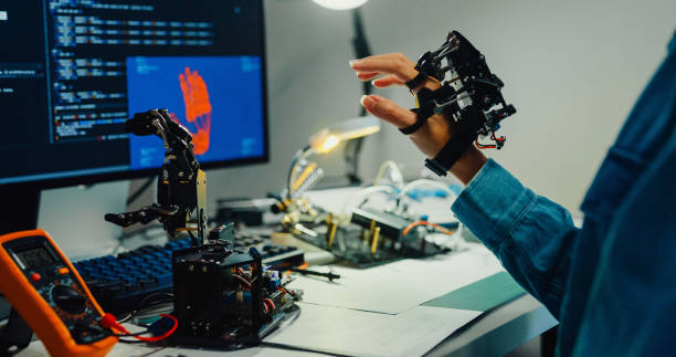 istock Closeup Young female engineer working late gestures towards robotic arm in tech lab at night. Machine learning, computer manufacturing, innovation and creativity. AI and Robotics Development. 2192647776