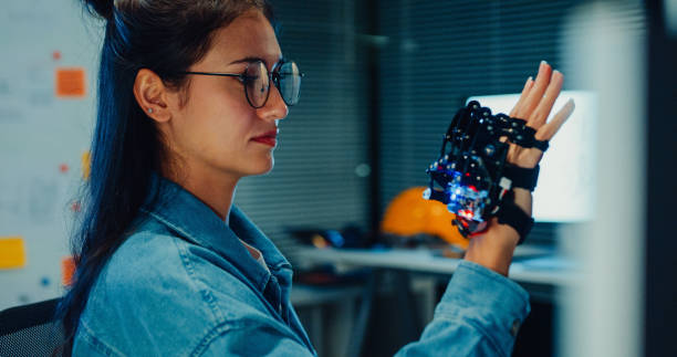 istock Young female engineer working late gestures towards robotic arm in tech lab at night. Machine learning, computer manufacturing, innovation and creativity. AI and Robotics Development. 2192648198
