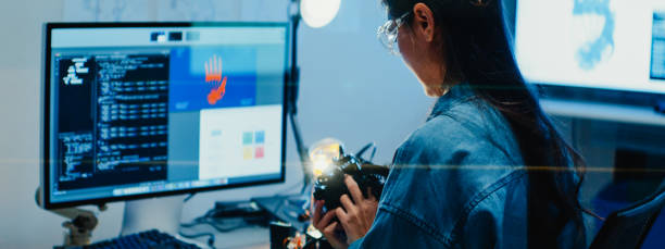 istock Young female engineer working late gestures towards robotic arm in tech lab at night. Machine learning, computer manufacturing, innovation and creativity. AI and Robotics Development. 2192648702