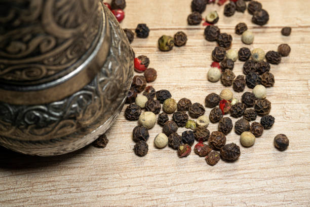 Spice grinder and peppercorns close up. Pepper mill with pepper mix on a wooden table.