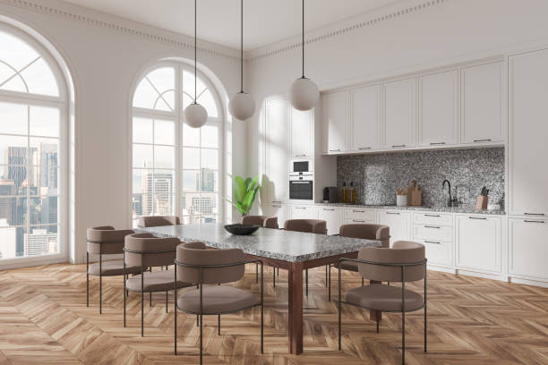 istock Spacious modern kitchen interior with large dining table and chairs, white cabinets, and panoramic windows offering a city view. 3D Rendering 2192656466