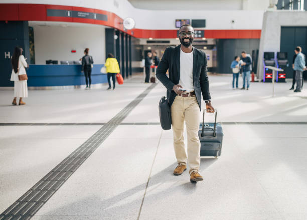 istock Businessman walking through airport terminal pulling suitcase and using smartphone 2192657461