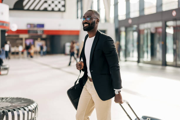 istock Businessman walking through airport terminal pulling suitcase and smiling 2192657808