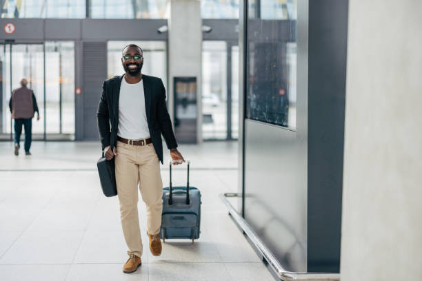 istock Businessman walking in airport terminal pulling suitcase and smiling at camera 2192658084