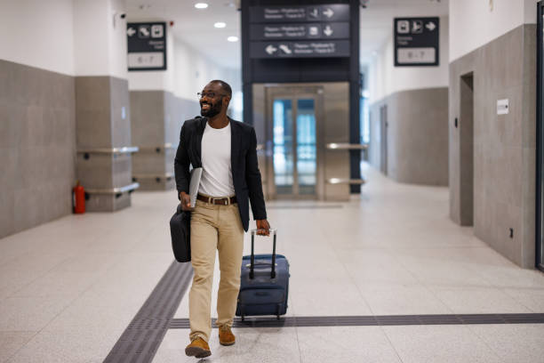 istock Businessman walking in airport terminal pulling suitcase and carrying laptop 2192658120