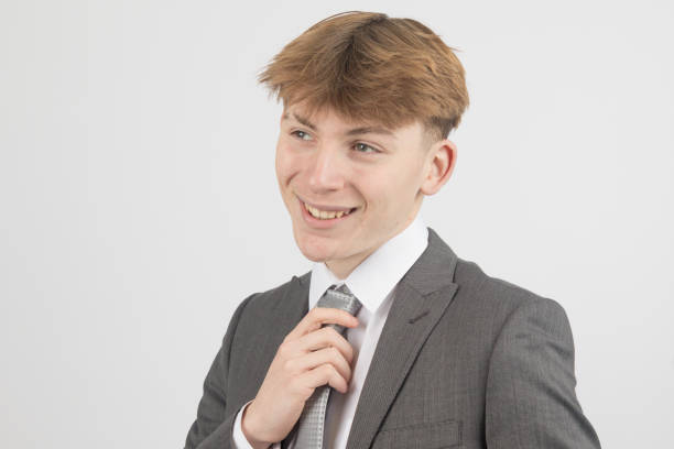 Happy Sixteen year old teenage boy wearing a suit, studio shot against a white background