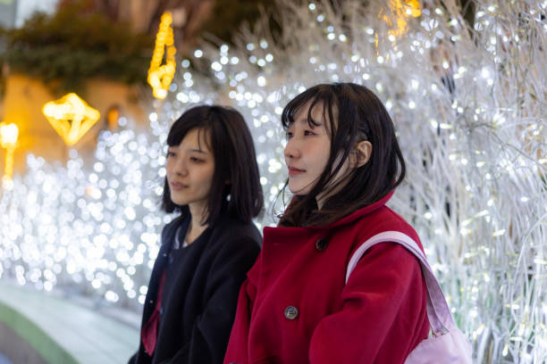 istock Female friends sitting on bench in Christmas lights 2192659613