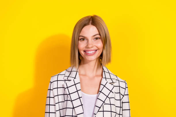 istock Confident young woman in stylish white jacket with grid pattern smiles against a vibrant yellow background, professionalism and charm. 2192661179