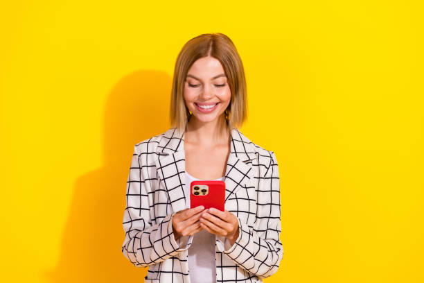 istock Charming young businesswoman in casual white jacket smiling while using smartphone against vibrant yellow background 2192661345