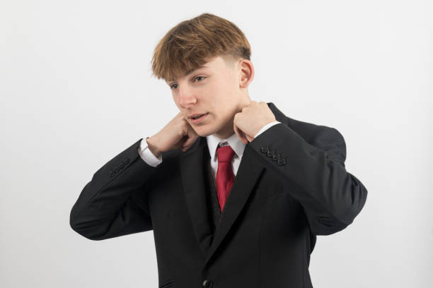 Sixteen year old teenage boy wearing a suit adjusting his collar, studio shot against a white background