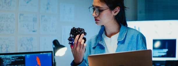 istock Young female engineer working late on a robotic arm prototype in tech lab at night. Machine learning, computer-aided manufacturing, innovation and creativity. AI and Robotics Development. 2192662421