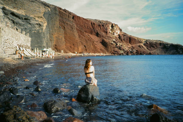 Cheerful woman resting on Red Beach on Santorini, Greece. Shot on camera film