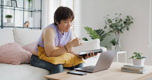 istock Gen Z Gay queer man non-binary sitting easy relax self study learn online happy work at home sofa. Asia people LGBT young adult guy WFH listen video call reskill upskill in MBA career job school class 2192663917