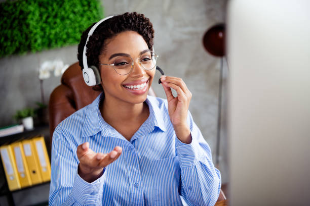 istock Young professional woman in a striped blouse working in a modern office setup with a headset, having a video call 2192665381