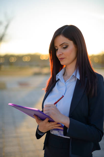 Young professional woman with red glasses writing on notepad in an urban setting, showcasing productivity and focus in a casual environment