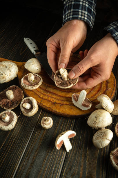 istock Hands skillfully prepare fresh mushrooms on a wooden board, surrounded by various types. A knife rests nearby, creating a cozy culinary atmosphere infused with earthy aromas 2192673092
