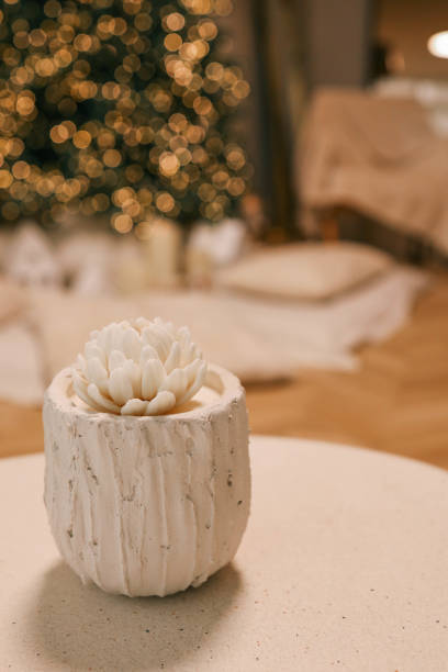istock Elegant white decorative candle resembling a blooming flower in a textured white holder, placed on a table with festive bokeh lights and a blurred Christmas tree in the background 2192676206