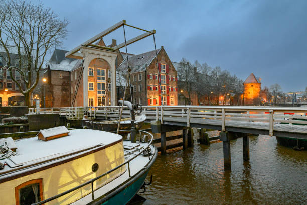 Zwolle snowy Thorbeckegracht during a cold winter morning with houseboats in the canal and the Broerenkerk church in the background. The rooftops and streets are covered in a thin layer of snow.