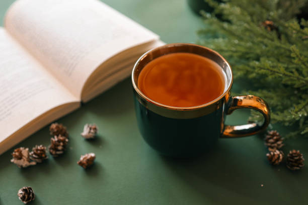 istock A cup of tea on a green surface with an open book, pinecones, and evergreen branches, creating a cozy and festive holiday atmosphere. Warm light and seasonal decor enhance the mood 2192676909