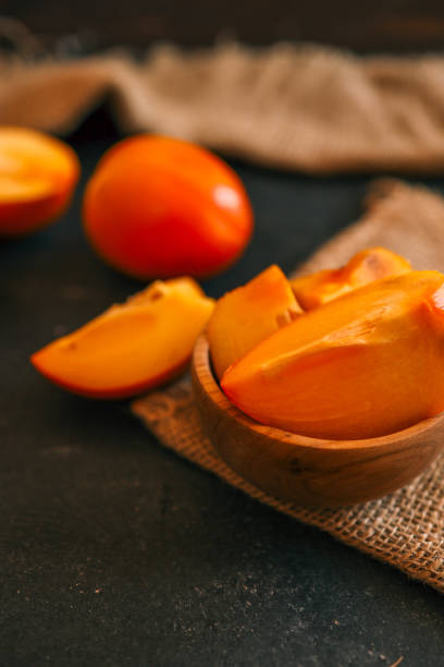istock Rustic composition with fresh persimmons in a wooden bowl and on a dark textured background, accented by burlap. Ideal for seasonal, culinary, and rustic lifestyle themes 2192677206