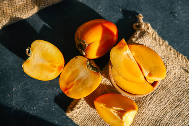 istock Sliced and whole persimmons arranged on a dark textured surface with natural light and burlap, showcasing vibrant colors and rustic simplicity. Perfect for food, seasonal, and healthy living themes 2192677216