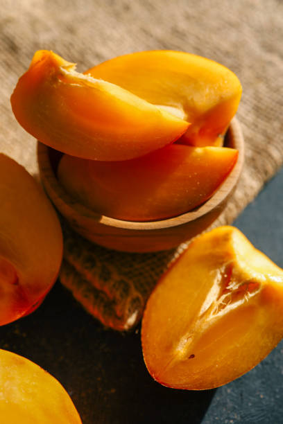 istock Sliced and whole persimmons arranged on a dark textured surface with natural light and burlap, showcasing vibrant colors and rustic simplicity. Perfect for food, seasonal, and healthy living themes 2192677218