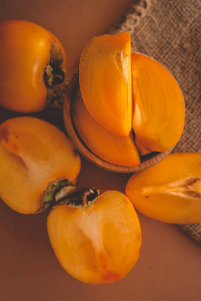 istock Fresh persimmons, both whole and sliced, placed on a rustic burlap cloth over a warm orange background, creating a cozy and autumn-inspired food arrangement 2192677219