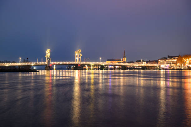 Evening view of the skyline with the Stadsbrug of the city of Kampen in Overijssel, The Netherlands. The lights of the city are reflected in the calm water while clouds are moving over the city in the sky.