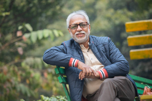 Portrait of smiling senior man in warm clothes sitting on bench in garden during winter