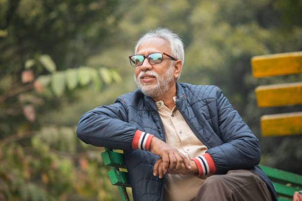 Portrait of smiling senior man in warm clothes sitting on bench in garden during winter
