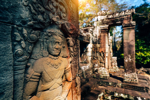 Historical art carvings of Angkor Wat temple surrounded by tropical trees with sunlight filtering through, highlighting details of the stone statues and the essence of Cambodian heritage and architecture.