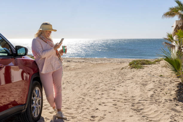istock Mature woman uses mobile phone by car on beach 2192686846