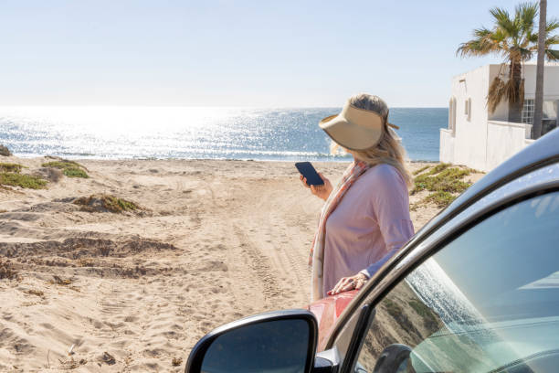 istock Mature woman uses mobile phone by car on beach 2192687132
